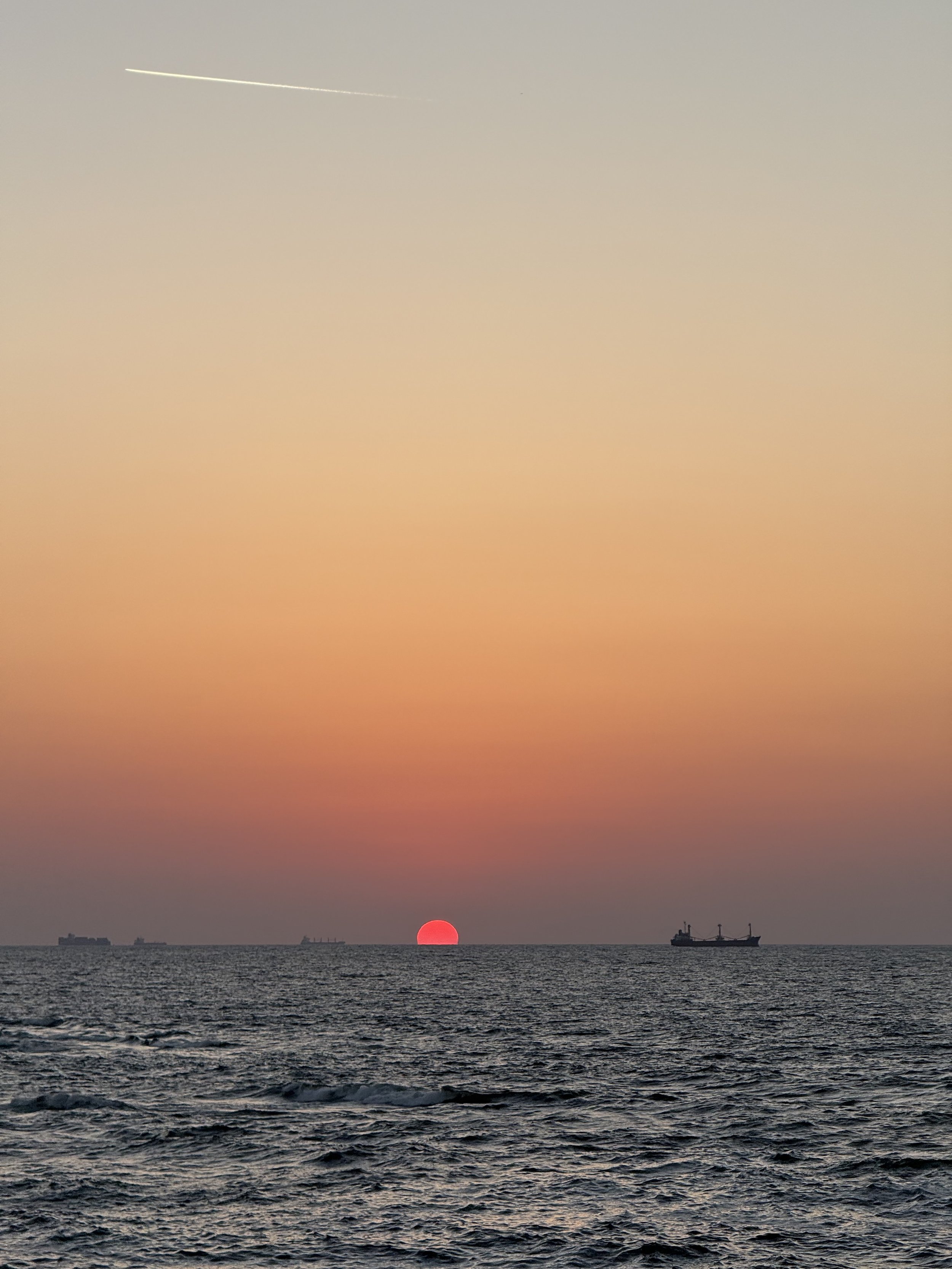 A pink sun sinking into the Mediterranean Sea off Alexandria, with cargo ships on the horizon.