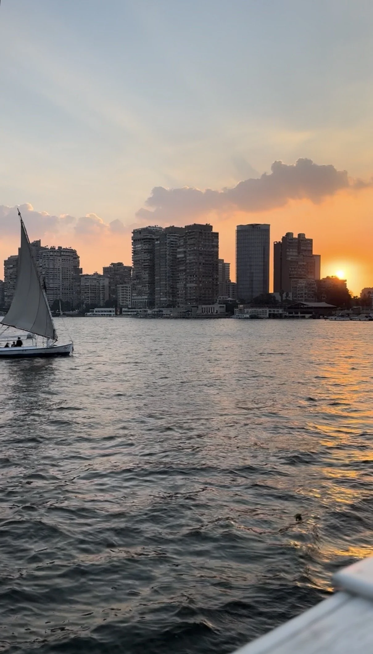 A felucca sailing past the Cairo skyline as the sun sets over the Nile, seen from a dinner cruise.