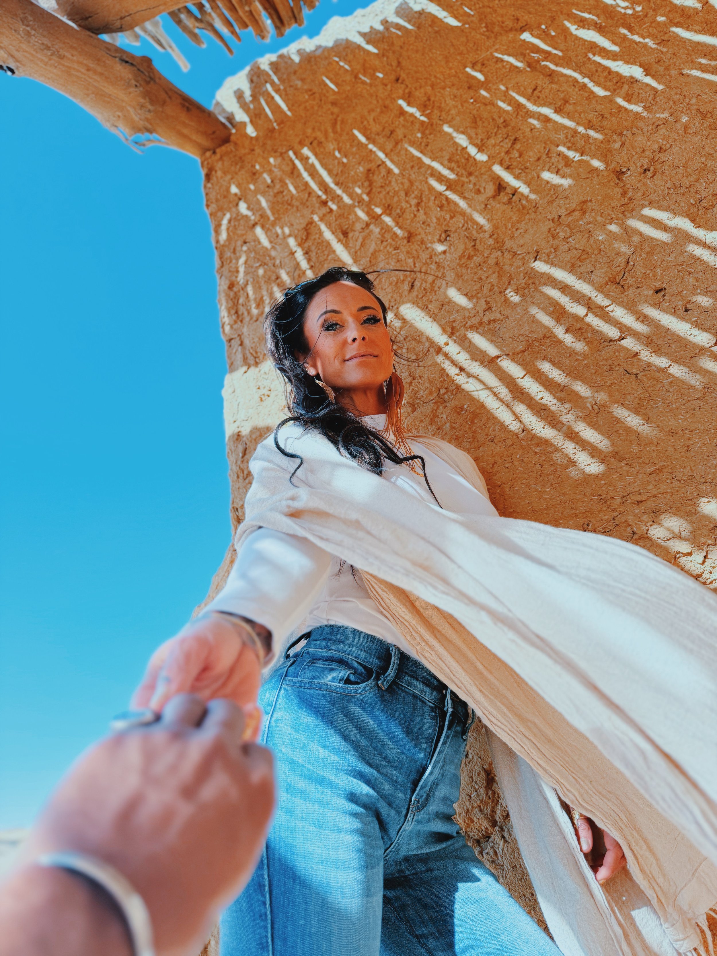 Jennifer of Takemet Tours reaching back for Mostafa’s hand beneath a palm-shaded roof at Wadi El Hitan.