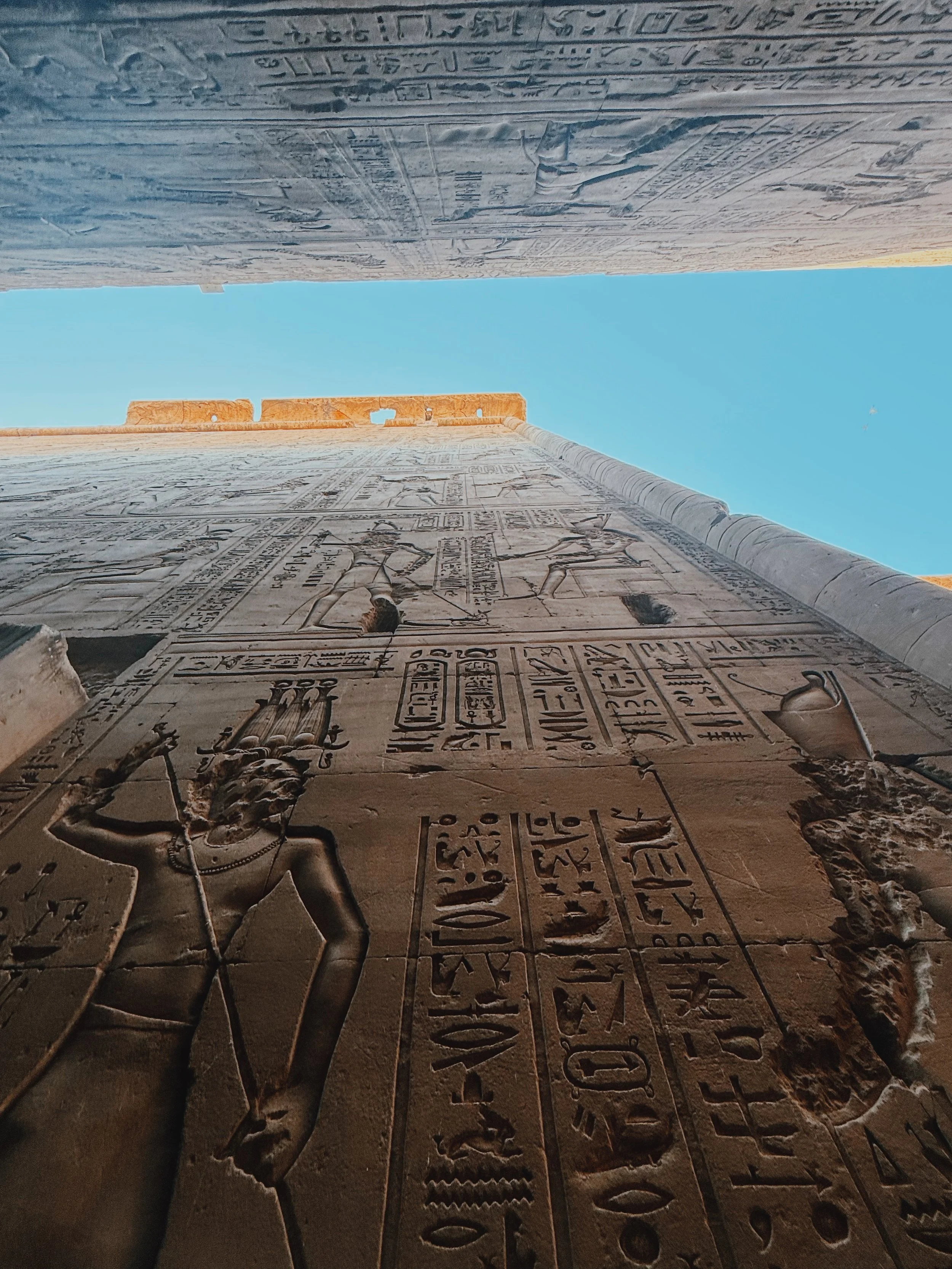 Looking up at towering carved walls and a strip of blue sky inside the Temple of Horus at Edfu.