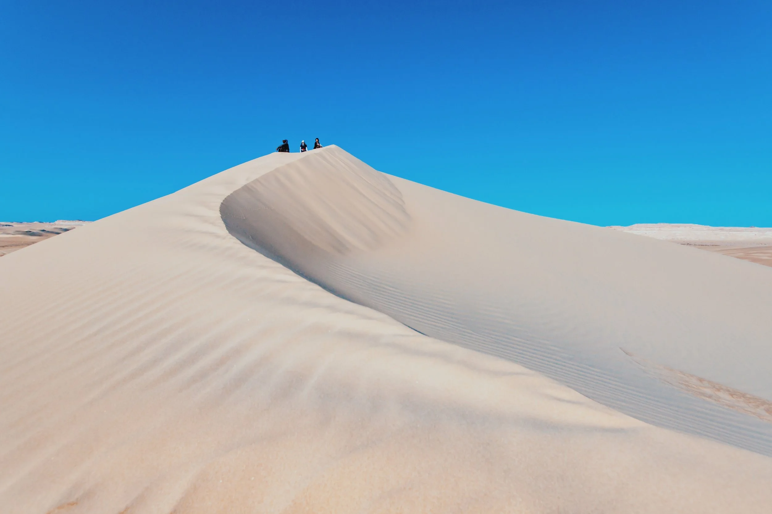 Three travelers on the crest of a towering dune in the Great Sand Sea near Siwa Oasis.