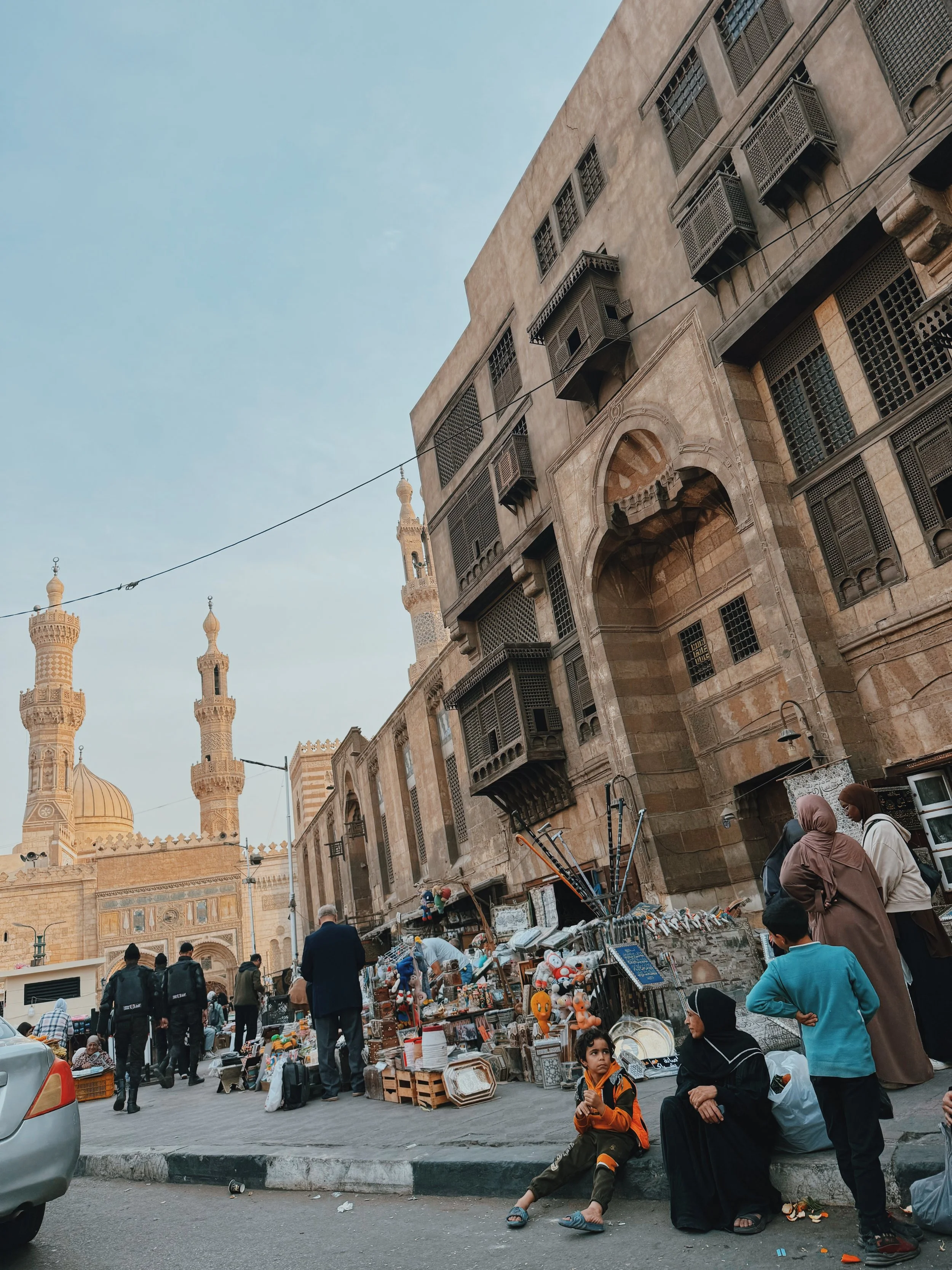 Mashrabiya-lined facades and minarets above a busy street market in Islamic Cairo.