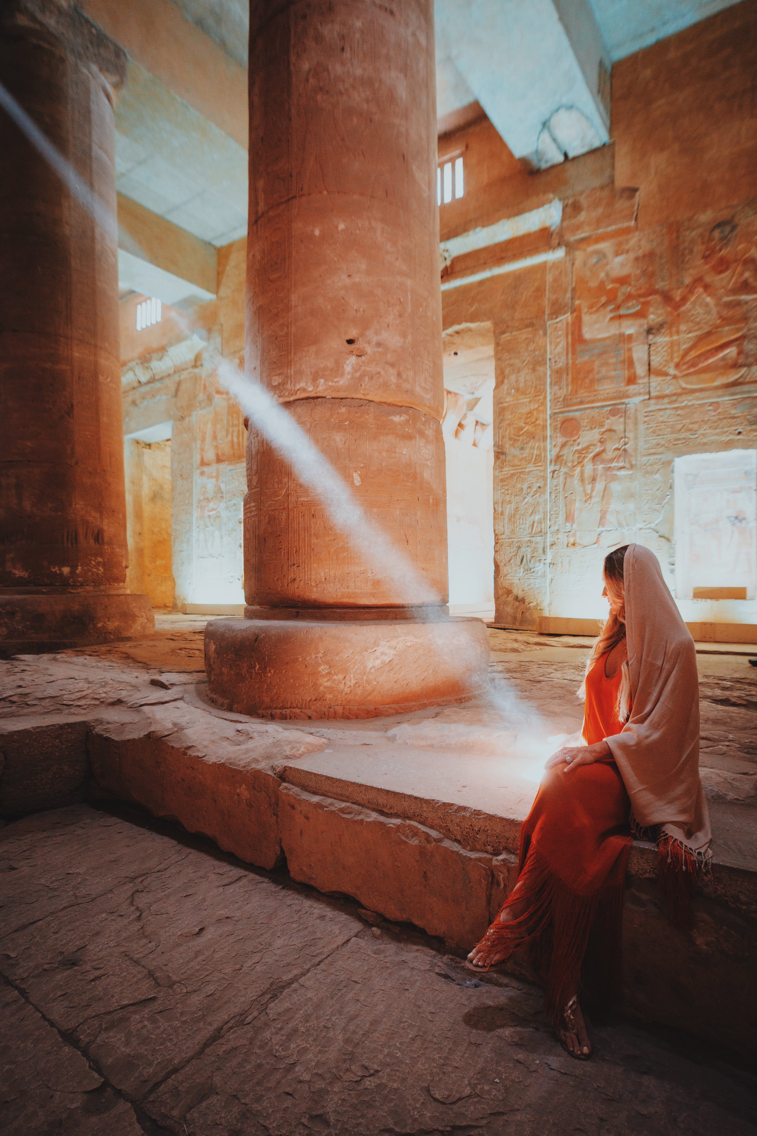 Jennifer of Takemet Tours seated in a shaft of sunlight among carved columns at the Temple of Seti I, Abydos