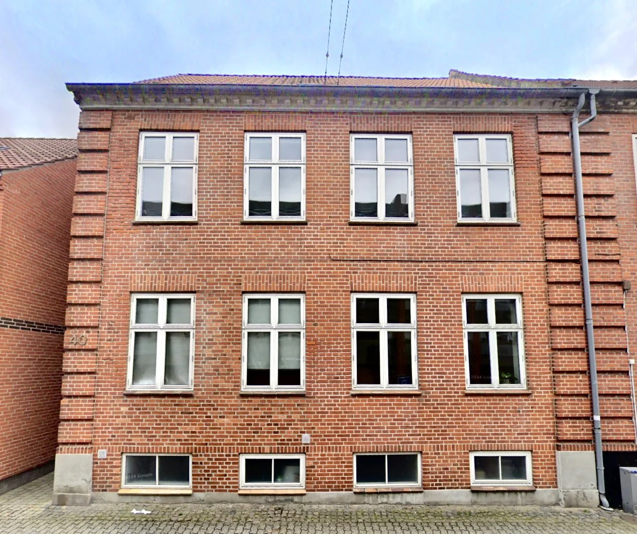 Fleretagers byfacade med røde mursten og hvidrammede vinduer, samt udendørs gade med brosten foran.