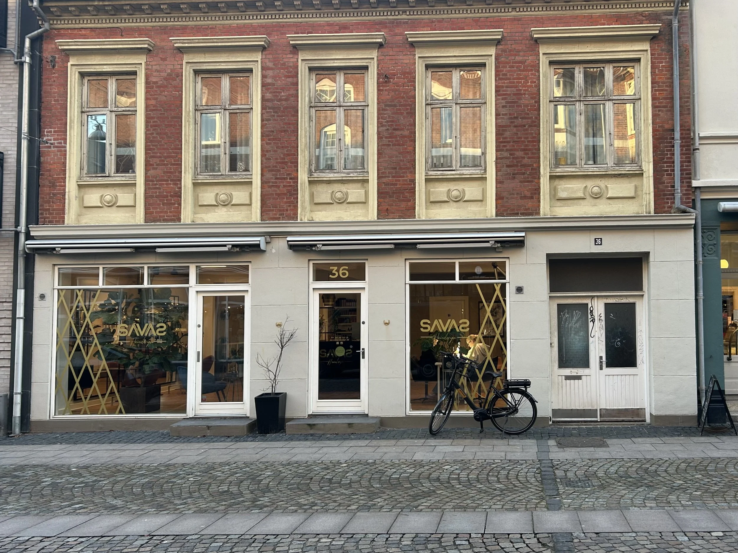 Facade af en butik med vinduer og døre, der har gule geometriske dekorationer, og nummer 36 over døren