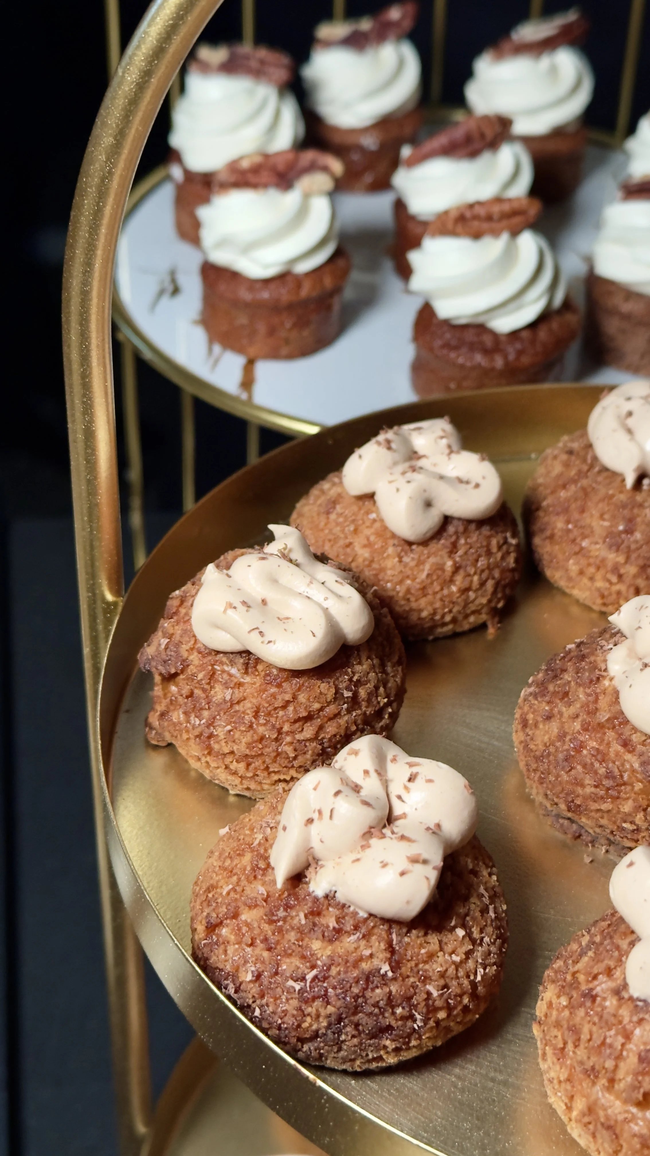 Desserts préparés, probablement des croquettes ou des elliptiques avec une garniture de crème ou de chocolat sur le dessus, présentés sur un plateau en or.