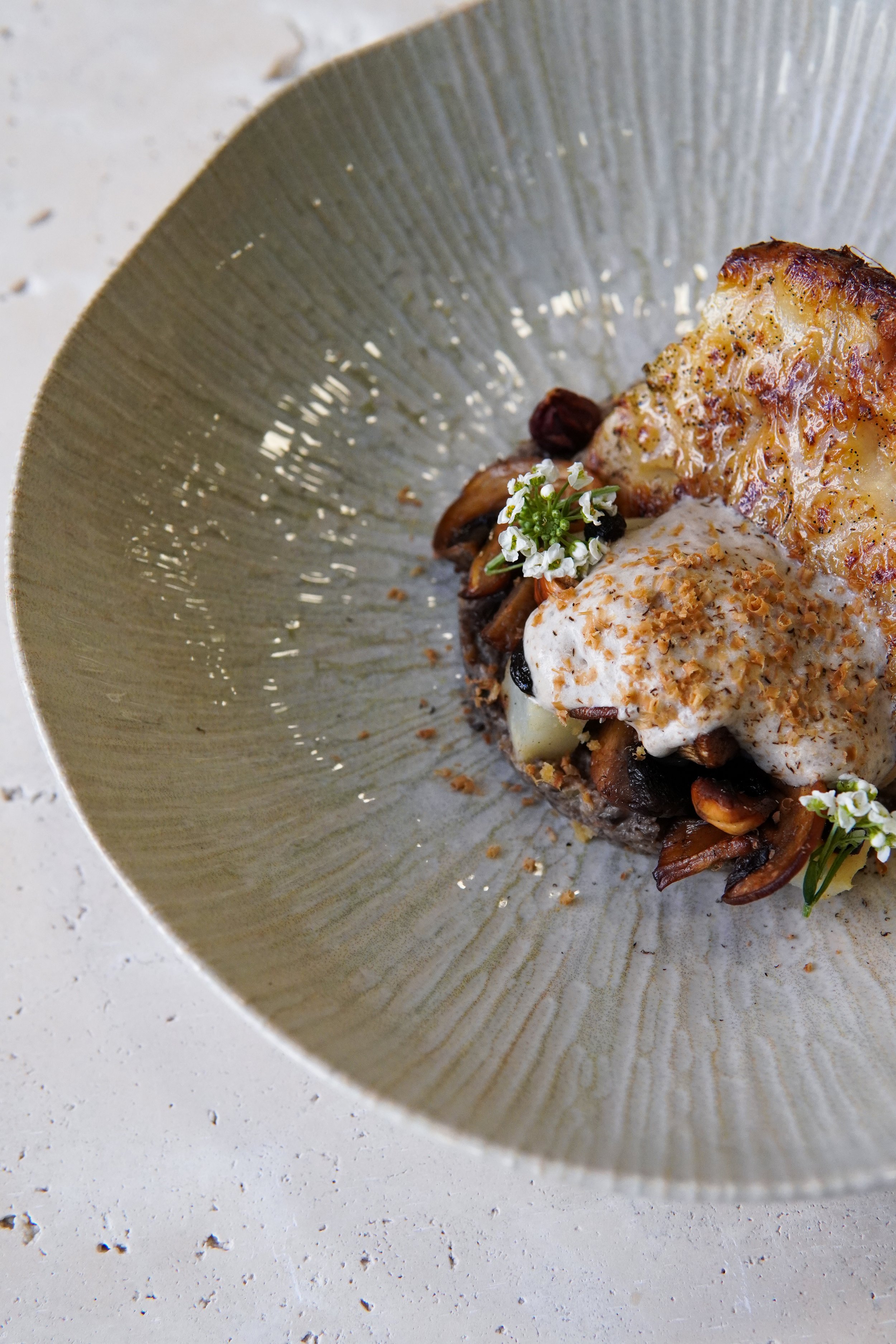 Plat appétissant avec un gratin rôti, champignons, garnitures crémeuses, fleurs comestibles et éclats croquants, servi dans une assiette élégante.