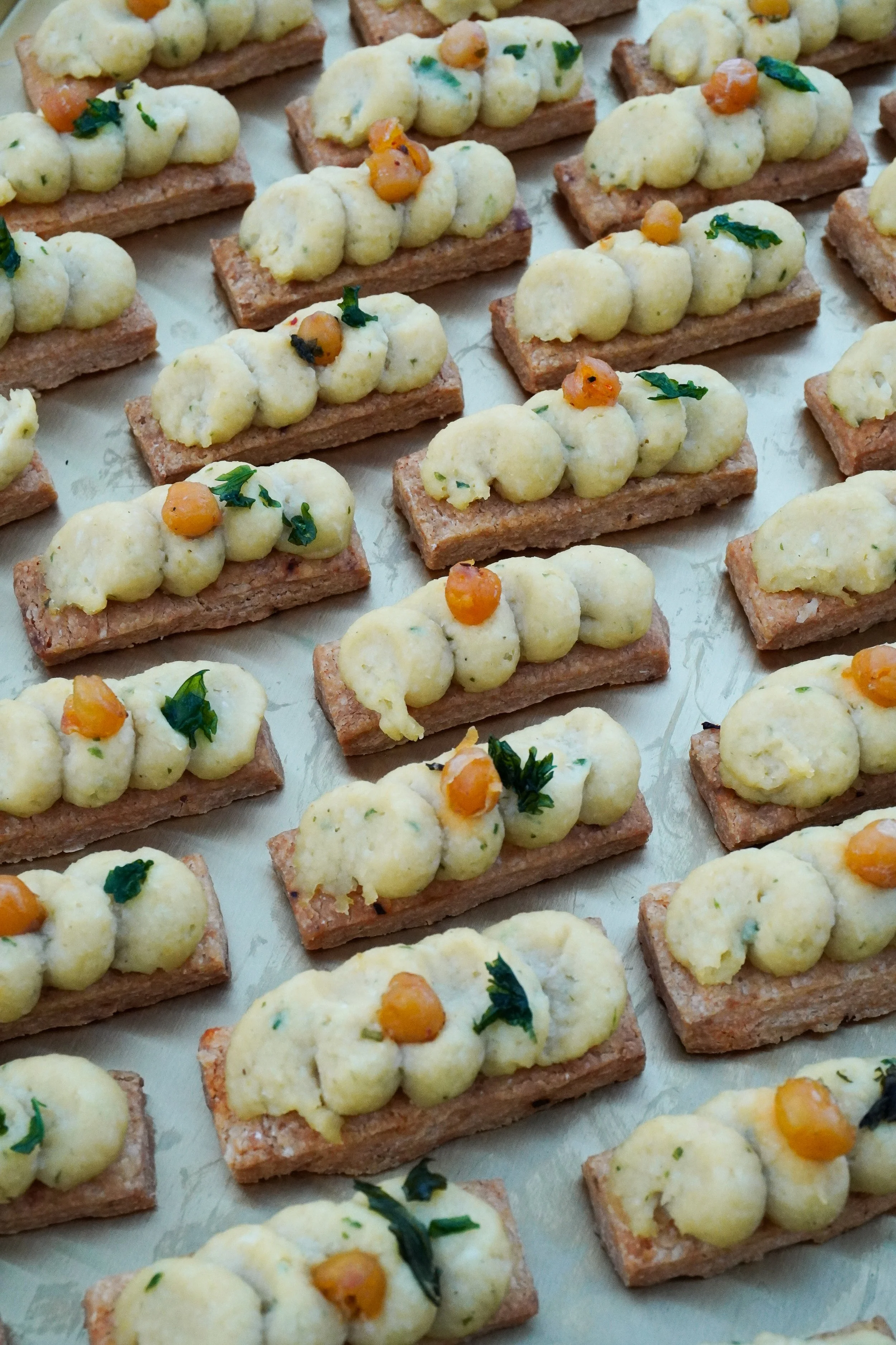 Petites tartines garnies de purée de pommes de terre, crème ou beurre, décorées avec de petits morceaux de légumes verts et de graines ou de pois chiches.