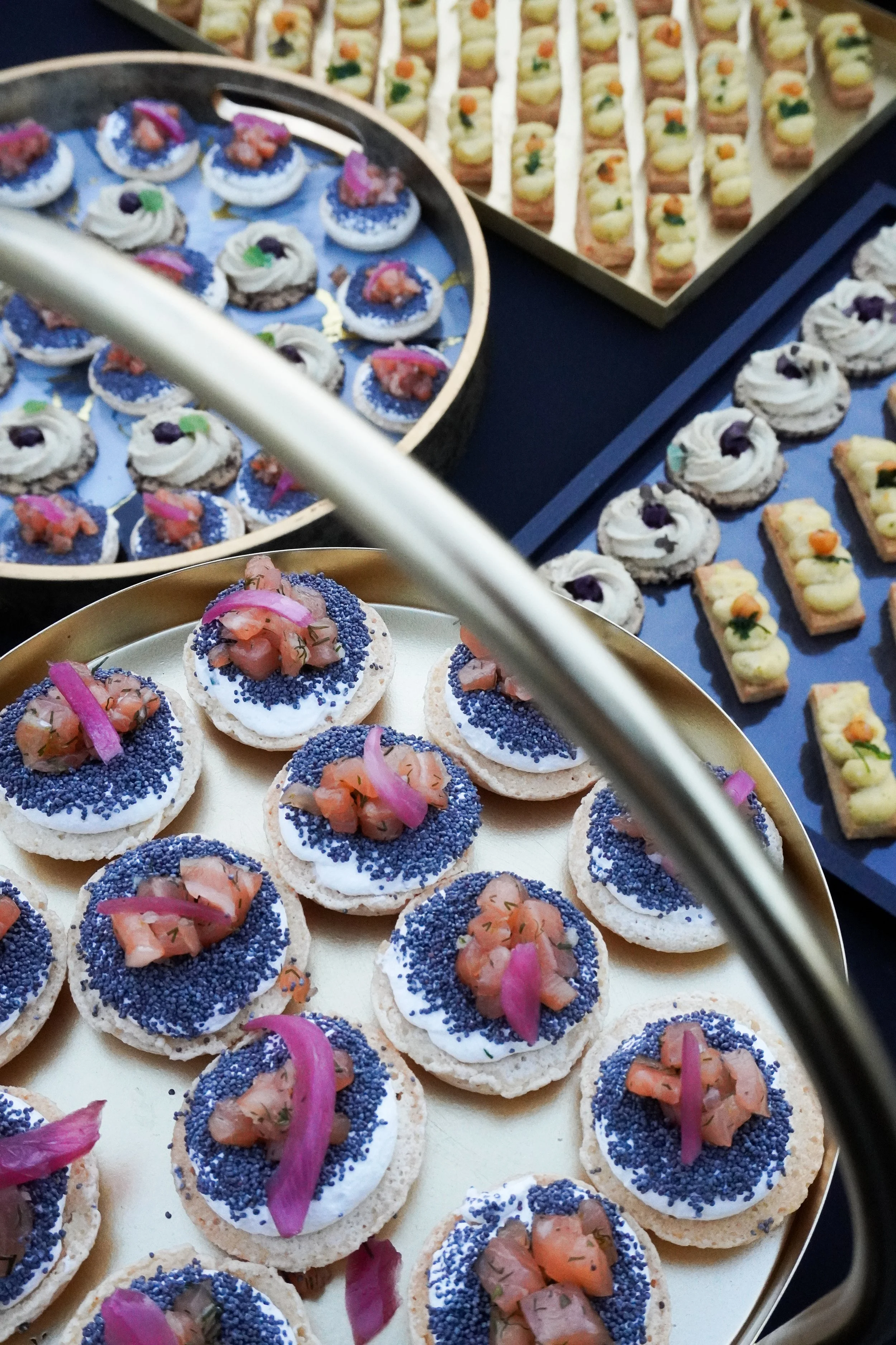 Assortiment de canapés et amuse-bouches décorés avec des garnitures colorées, présenté sur des plateaux lors d'un événement gastronomique.