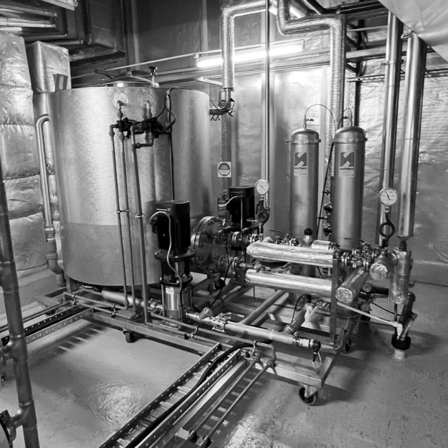 Industrial machinery with tanks, pipes, and gauges in a basement or utility room.