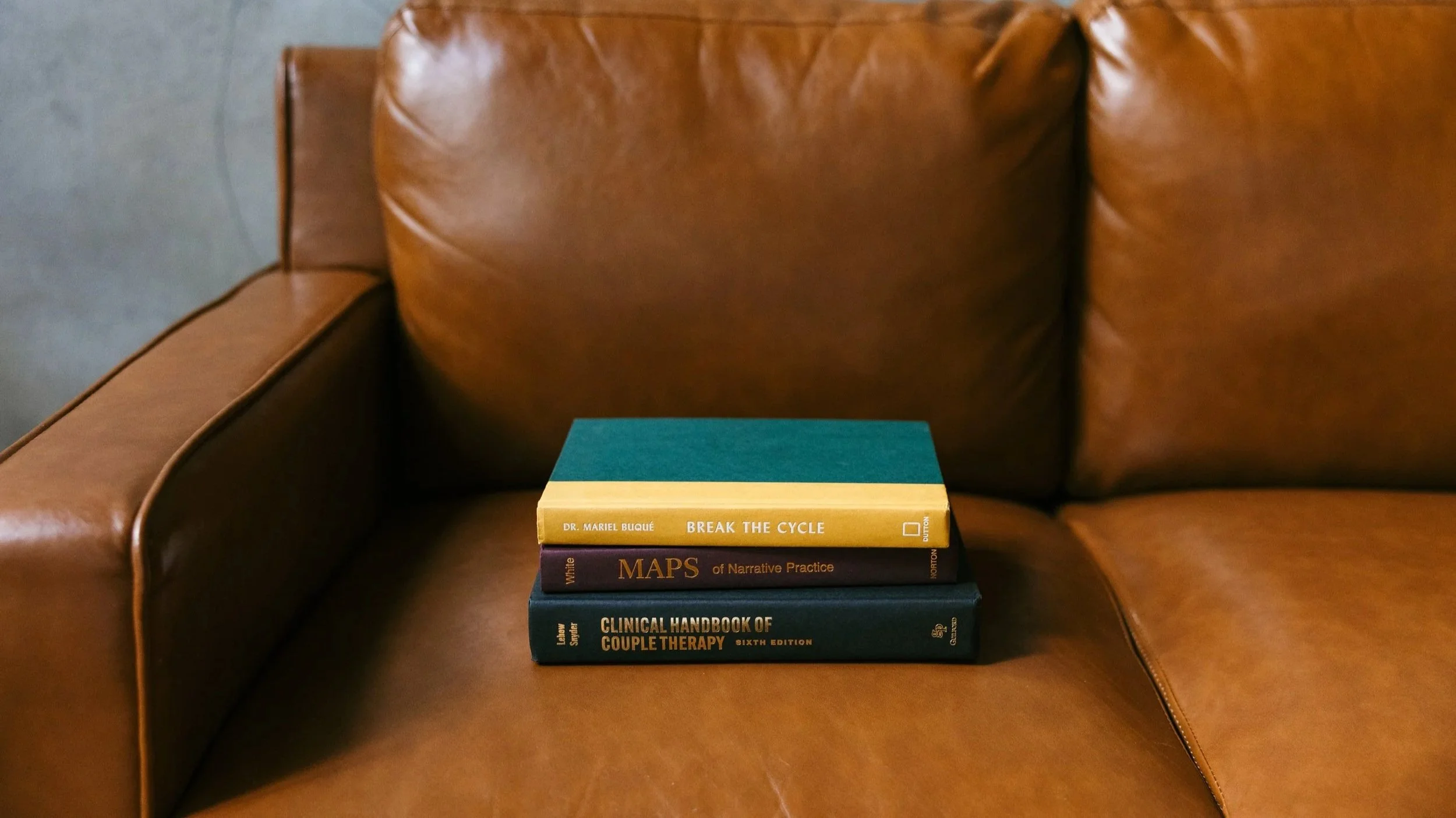 Stack of therapy and counseling books on a leather couch, representing individual counseling at Hanks Therapy Co. in Nashville and Brentwood for young adults, teens, healthcare workers, and people seeking support for anxiety, burnout, stress, adhd.