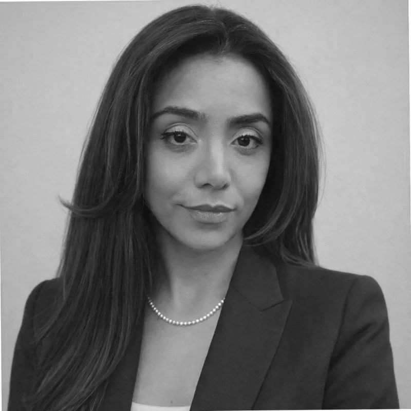 Black and white portrait of a woman with long hair, wearing a blazer and a pearl necklace.