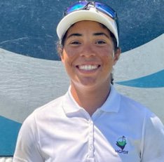 A young woman with a white cap and sports sunglasses smiling in front of a blue and white background, wearing a white sports shirt with a logo.