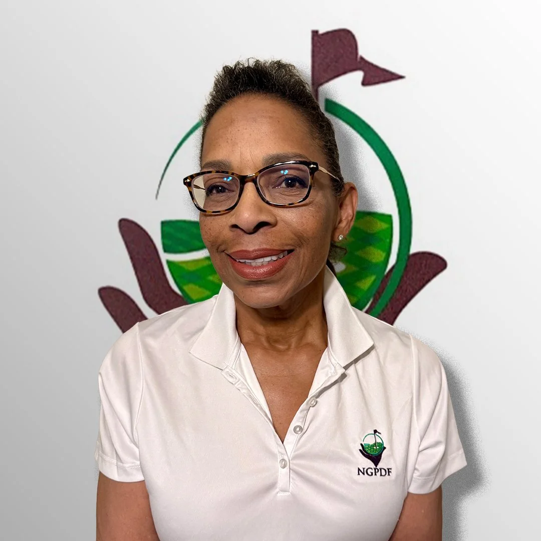 A smiling woman with glasses and earrings, wearing a white polo shirt with a logo that has the letters 'NGPDF' and a graphic of a cup and leafy design, standing in front of a wall with a circular green and maroon graphic logo.