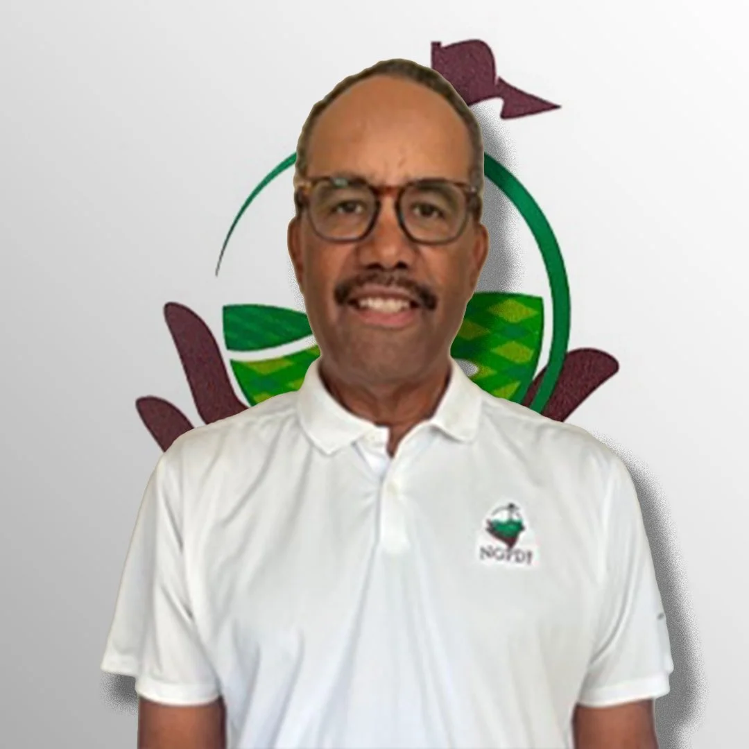 A man with glasses and a mustache wearing a white polo shirt with the logo of NSNDOT, standing in front of a logo featuring green leaves and purple hands.