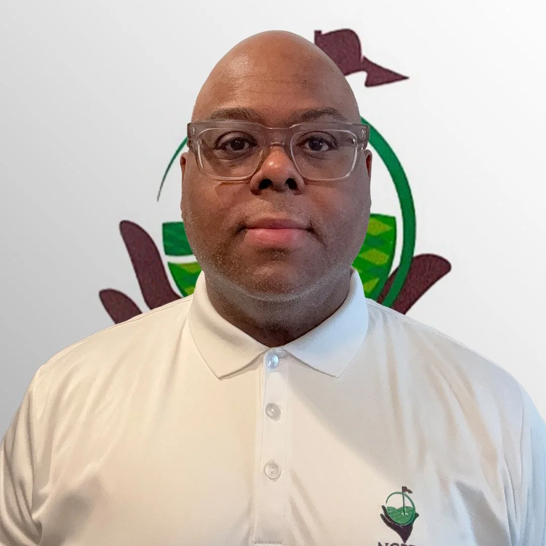 A man wearing glasses and a white polo shirt with the NGPDF logo, standing in front of a white wall with a colorful logo featuring a hand, a globe, and a flag.