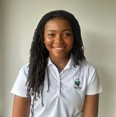 A young woman with long dreadlocks wearing a white polo shirt, smiling against a plain light-colored background.