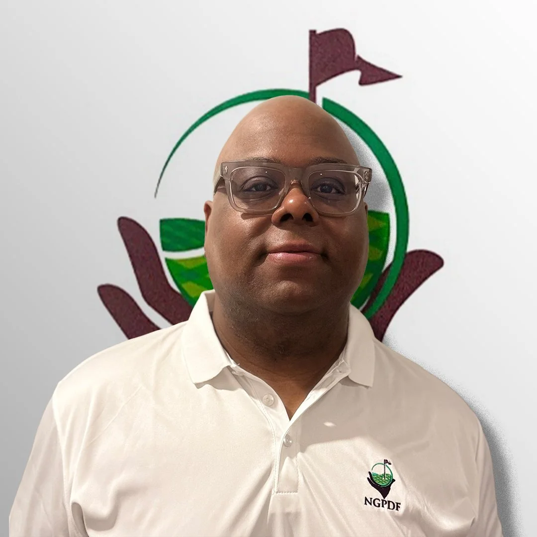 A man wearing glasses and a white polo shirt with the NGPDF logo, standing in front of a white wall with a colorful logo featuring a hand, a globe, and a flag.