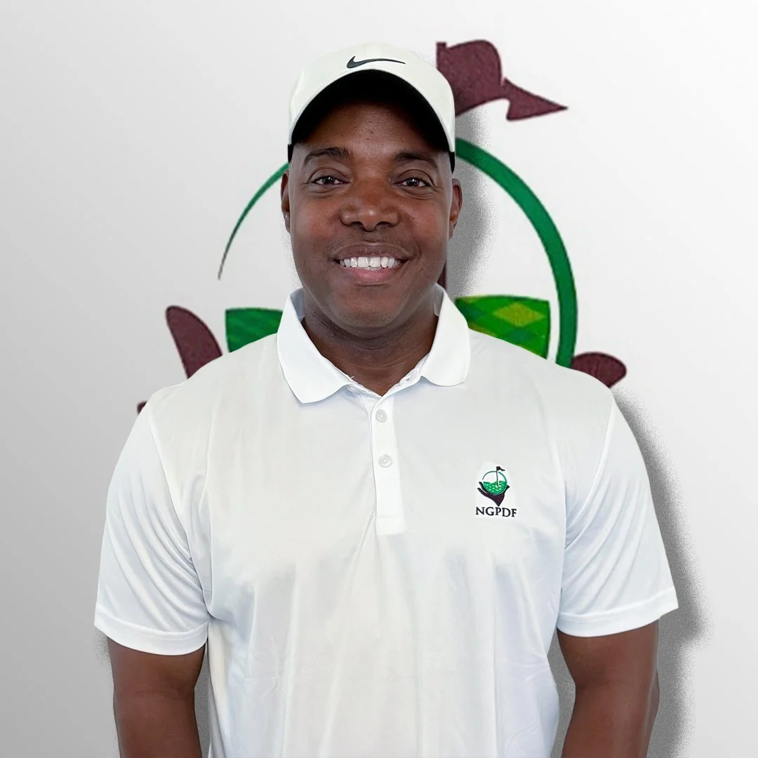 Smiling man wearing a white cap and white polo shirt with a logo, standing in front of a wall with a logo in the background.