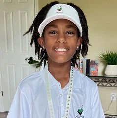 Young girl wearing a white visor and a white shirt, smiling indoors.