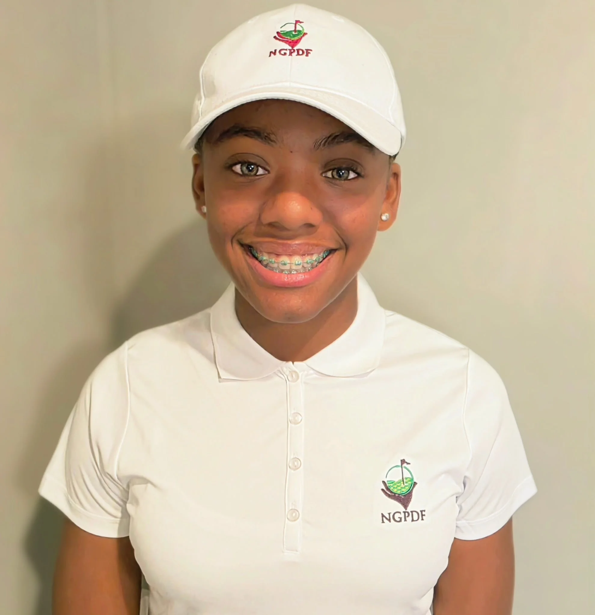 Young woman smiling outdoors holding a certificate of achievement, standing in a garden area with a white picket fence and trees.