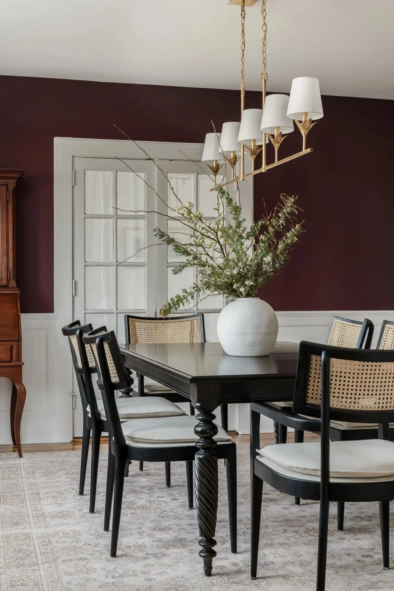 Bold colors with brass linear chandelier accented by black dining room table and natural cane backed chairs to enhance a refreshed luxury dining room redesign