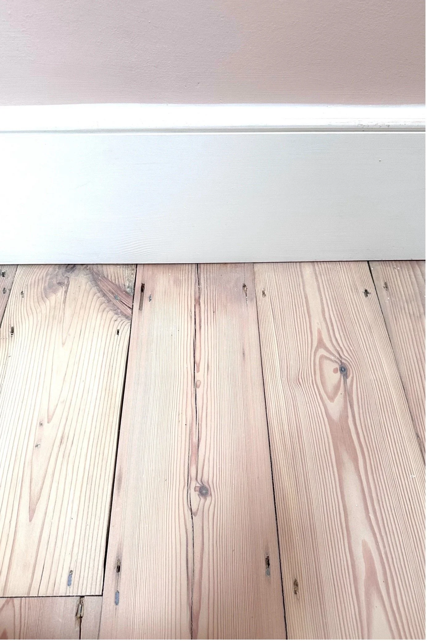 Detail shot of reclaimed pine flooring showing natural wood knots, installed next to white trim.