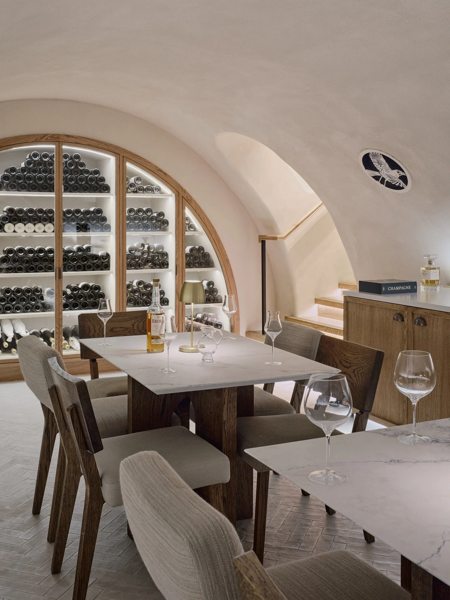 Cellar tasting room beneath an arched rendered ceiling, with a wine display in the arch, a dining table and chairs, and a laser-cut joinery grille.