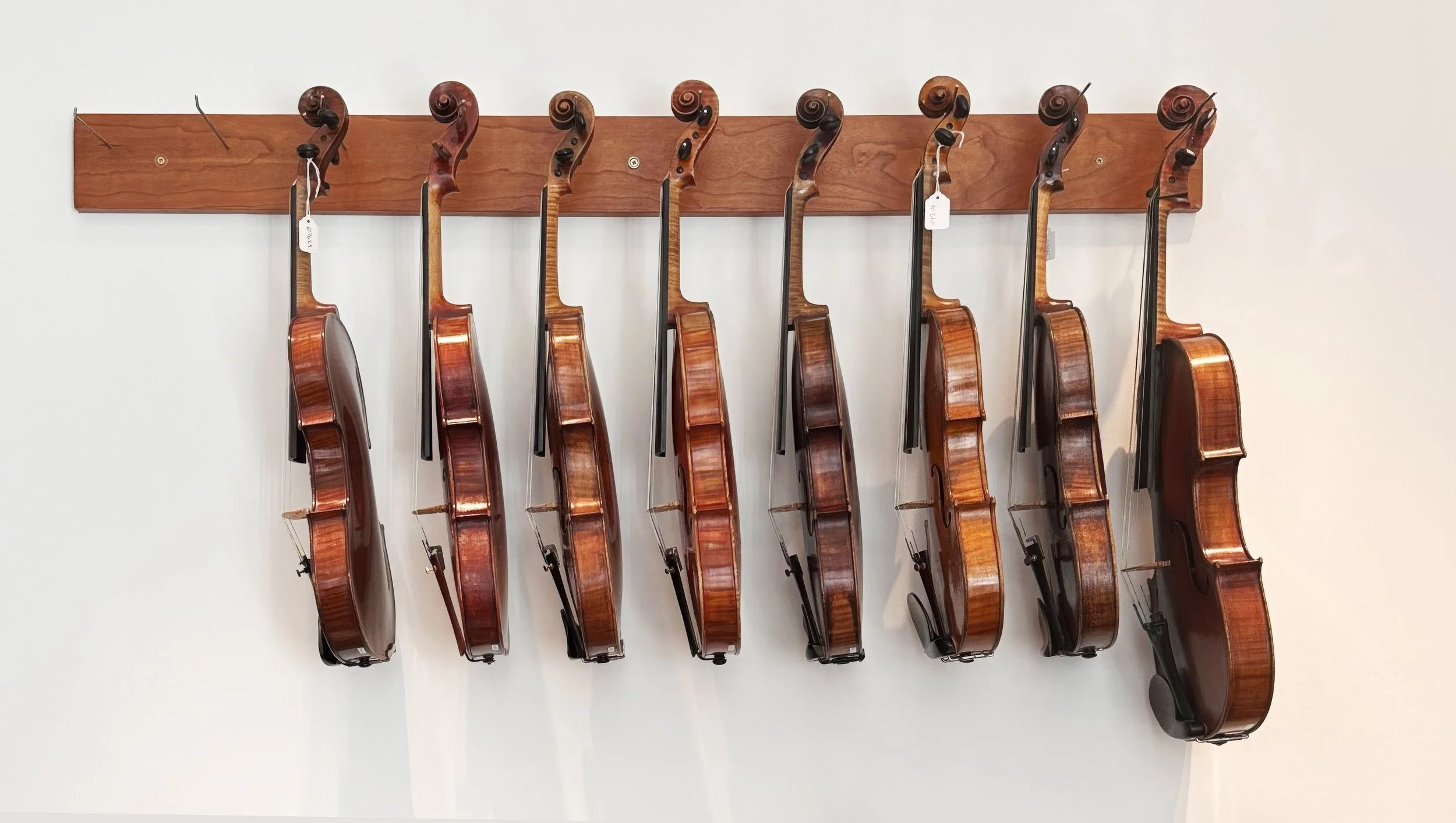 Row of violins hanging in order from a timber display rail at Tarisio London