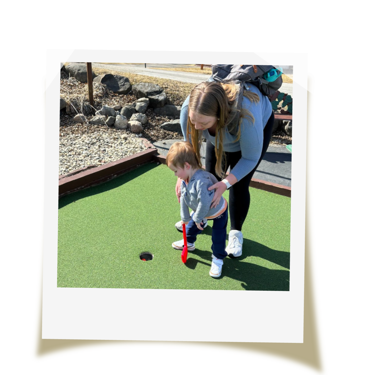 A woman helping a young boy putt on a mini golf green during daytime.
