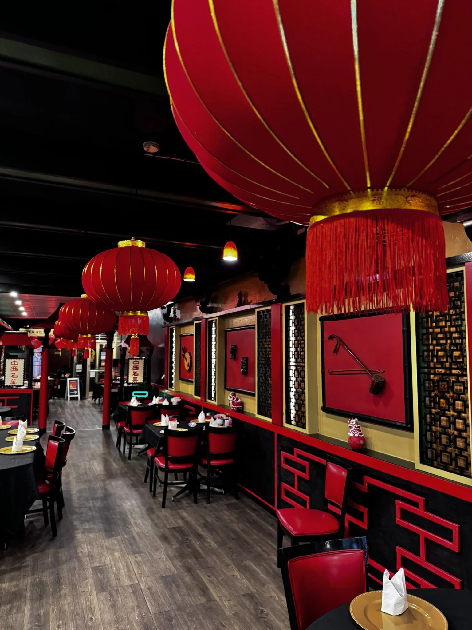 Interior of a Chinese restaurant decorated with red lanterns, black and red furniture, and traditional Chinese wall art.