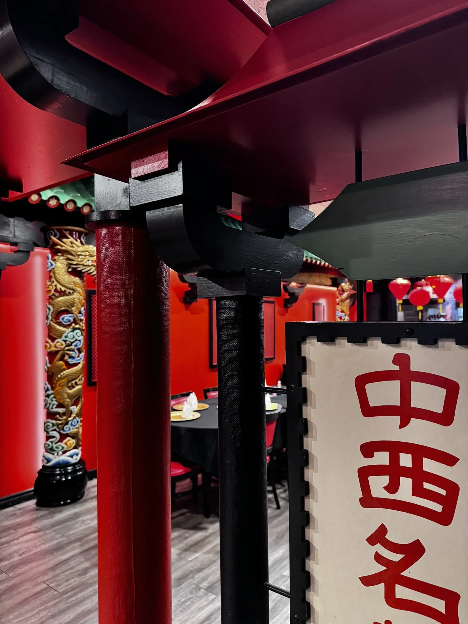 Close-up of decorative Chinese artifacts, including a black dragon sculpture, red pillars, and a sign with red Chinese characters, in a restaurant or cultural space.