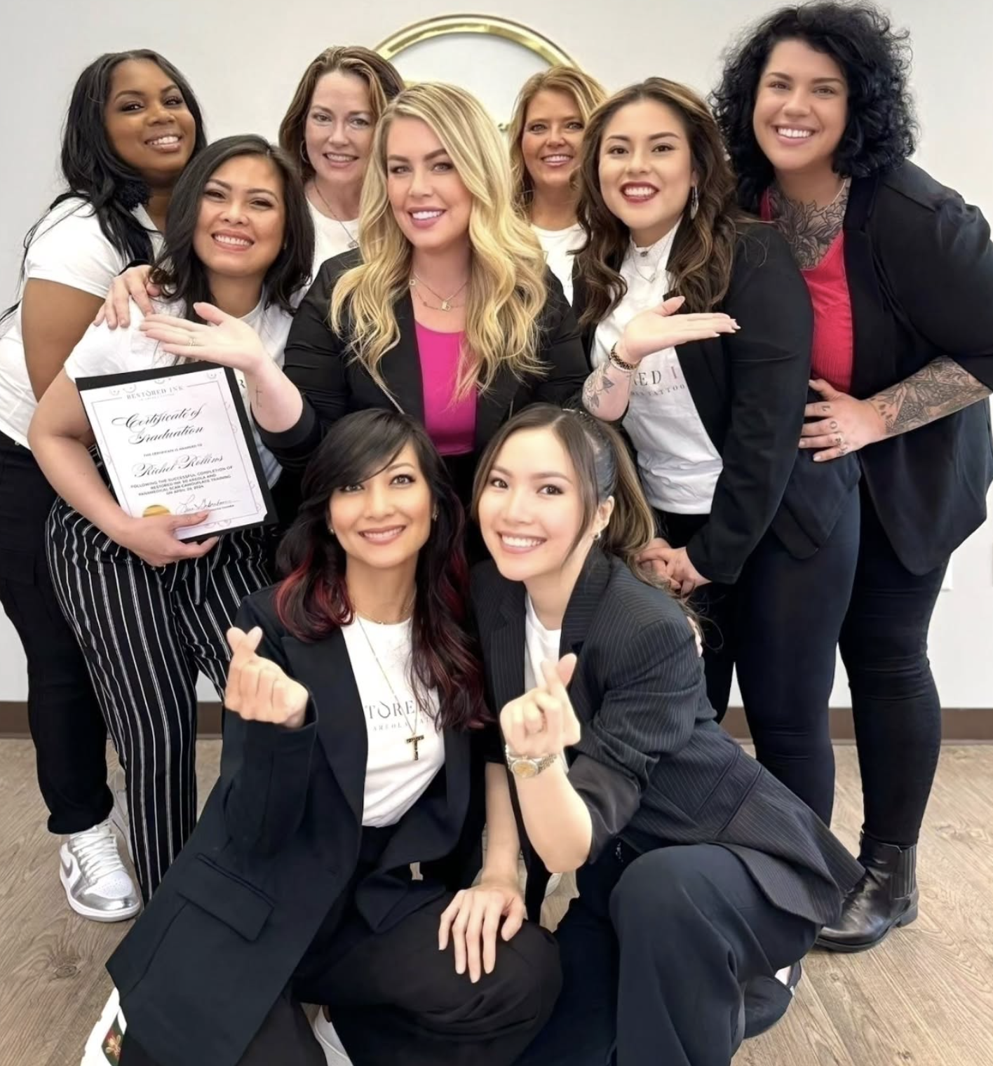 Group of diverse women celebrating a graduation, some holding certificates, smiling, making heart and finger gestures