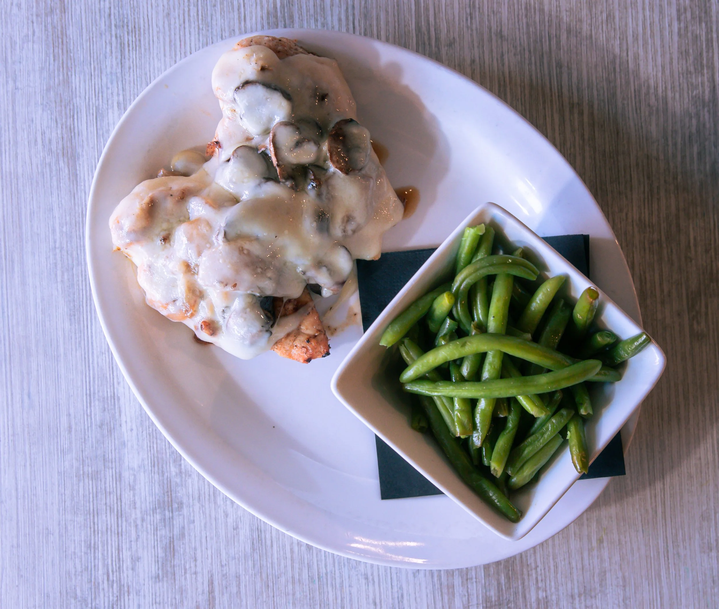 Plate with chicken and mushroom gravy, and a bowl of green beans.