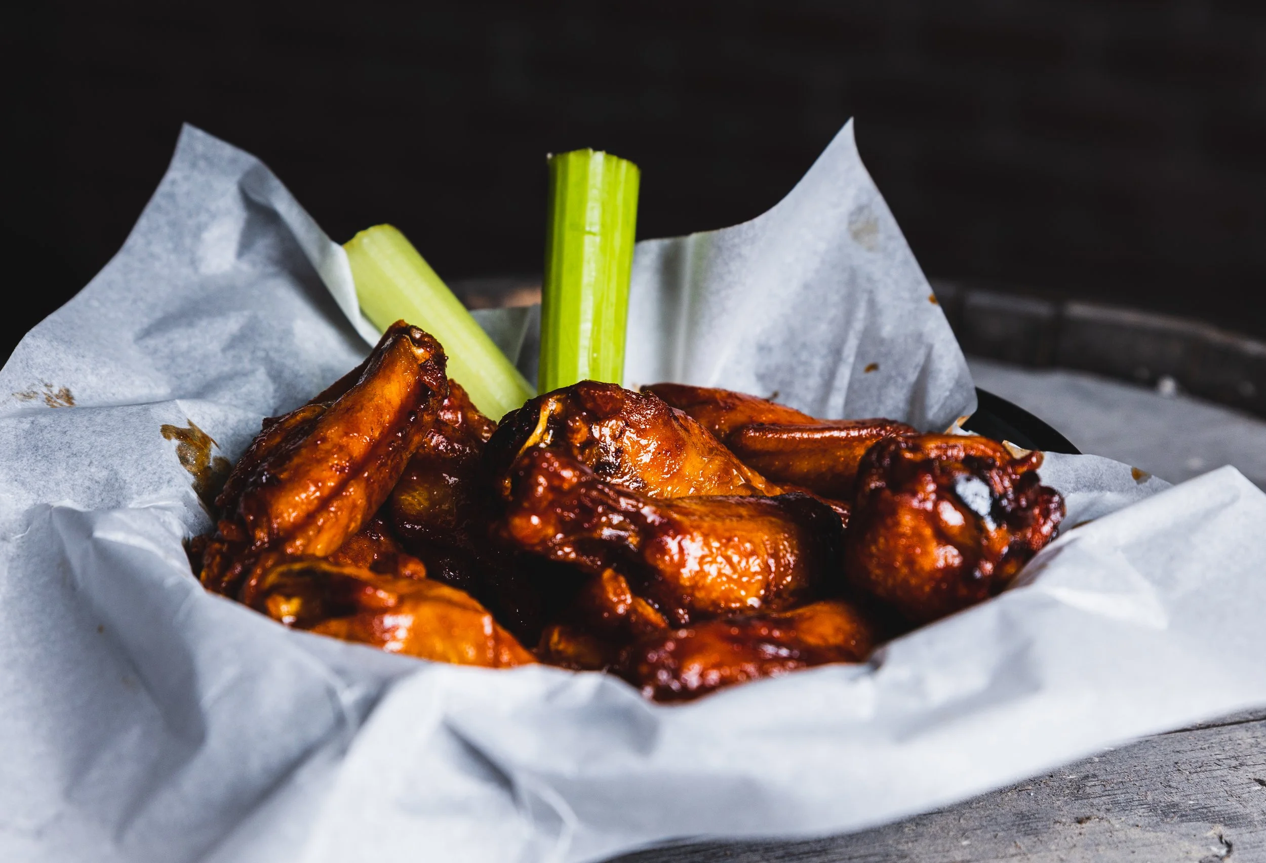 Barbecue chicken wings with celery sticks on paper in a basket.