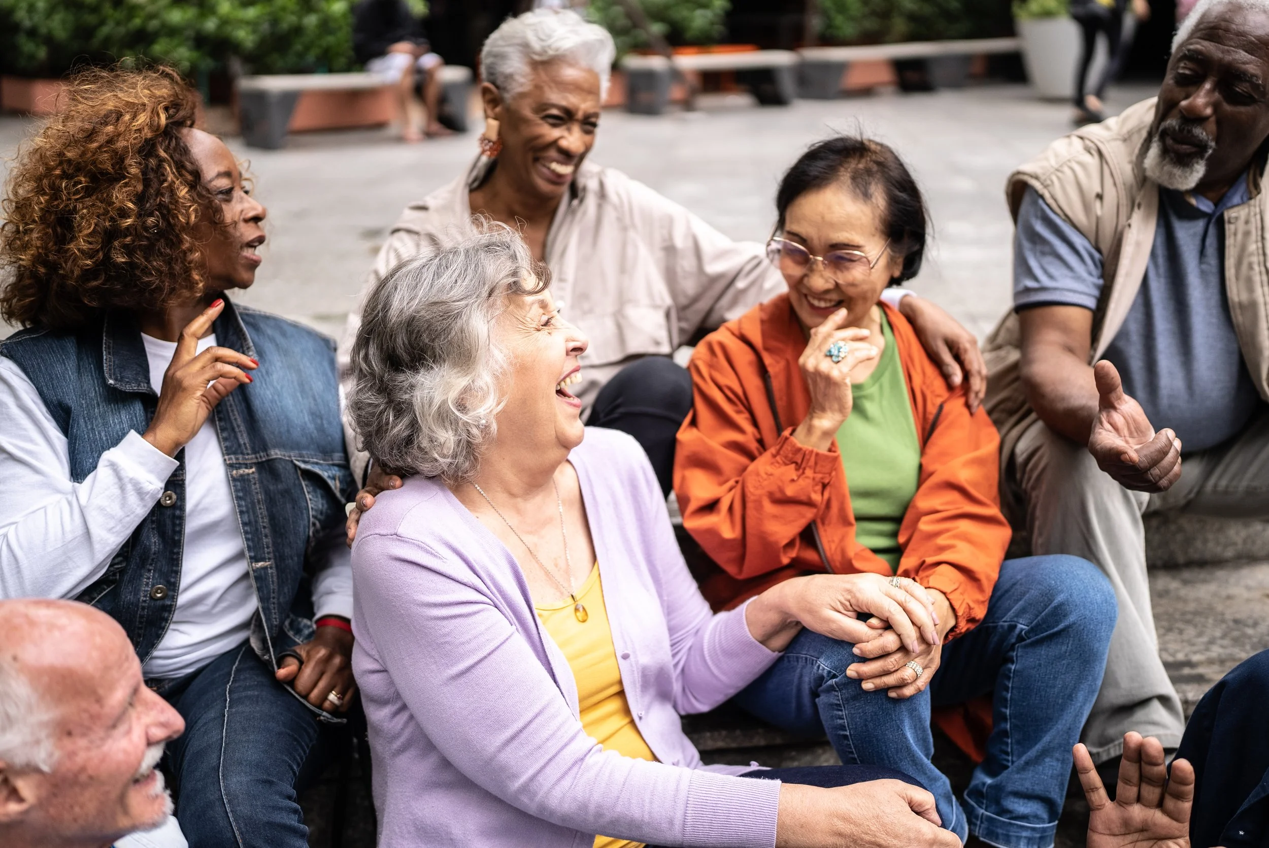 Group of diverse older adults sitting on steps outdoors, laughing and enjoying each other's company.