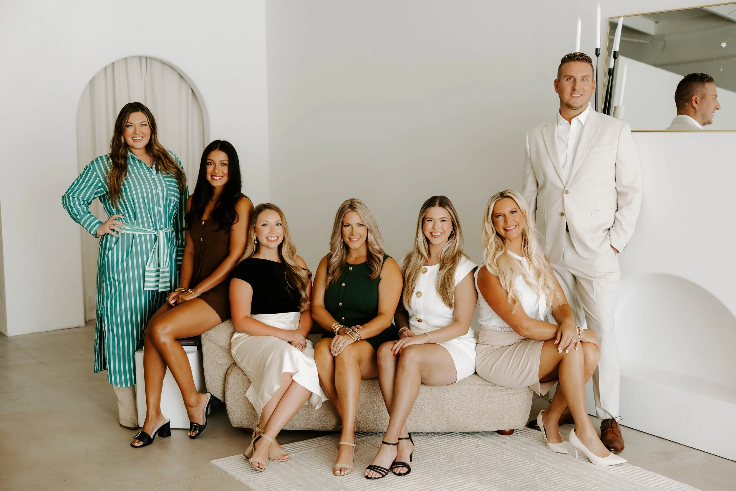 The 7 members of the Provision Realty Group team sitting and standing around a beige couch in a beige room