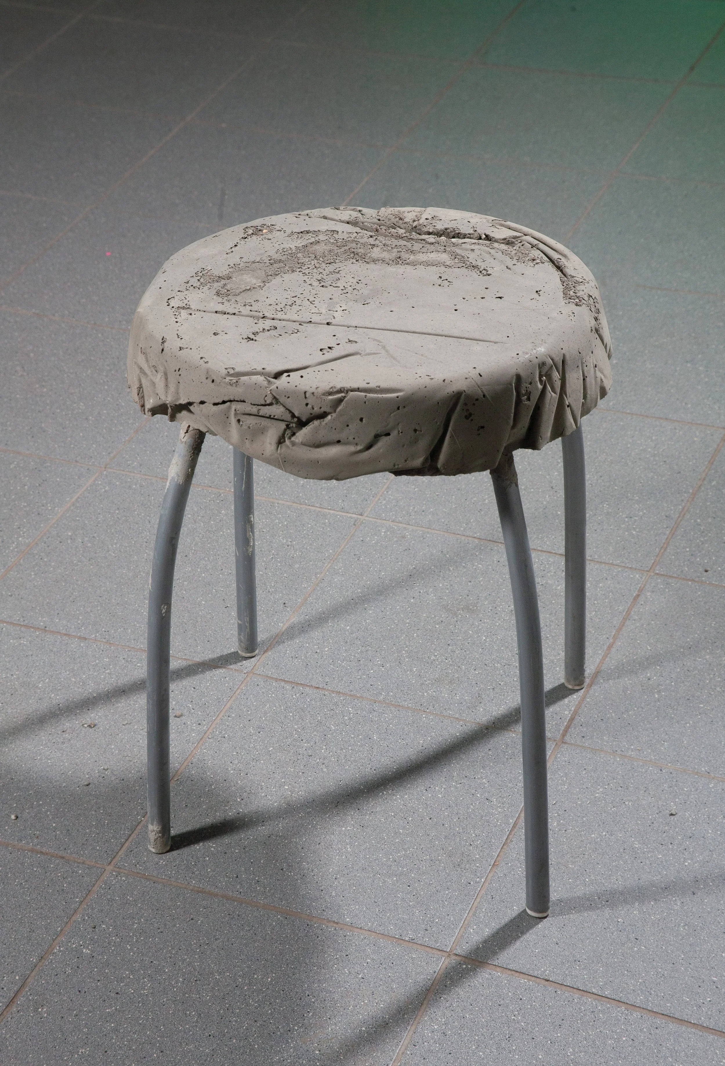 A worn, dusty stool with a crumpled paper cover on top, standing on a gray tiled floor.