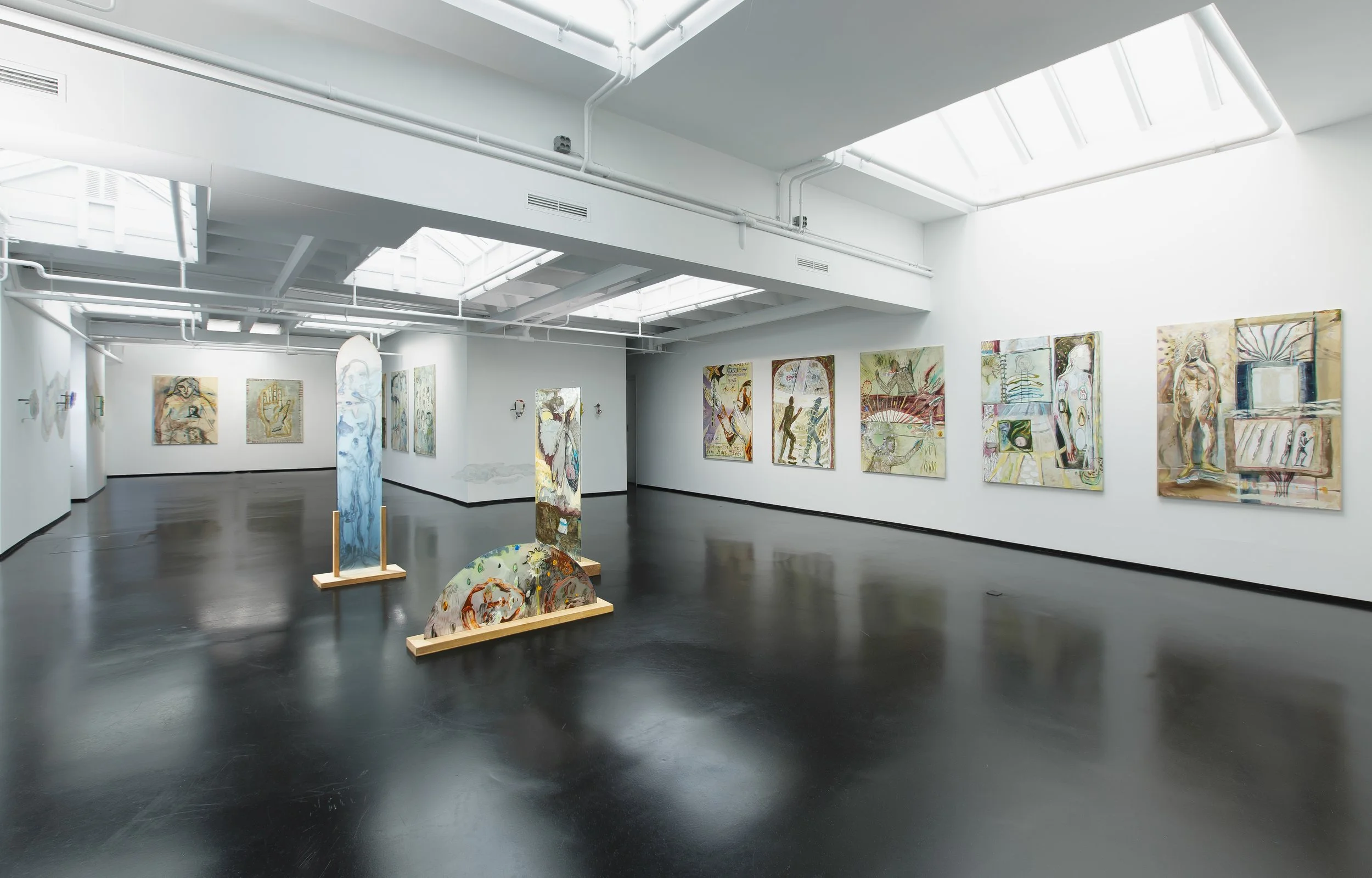 Modern art gallery with white walls and black floors, displaying various abstract paintings and sculptures, including painted panels and painted decorated stones.