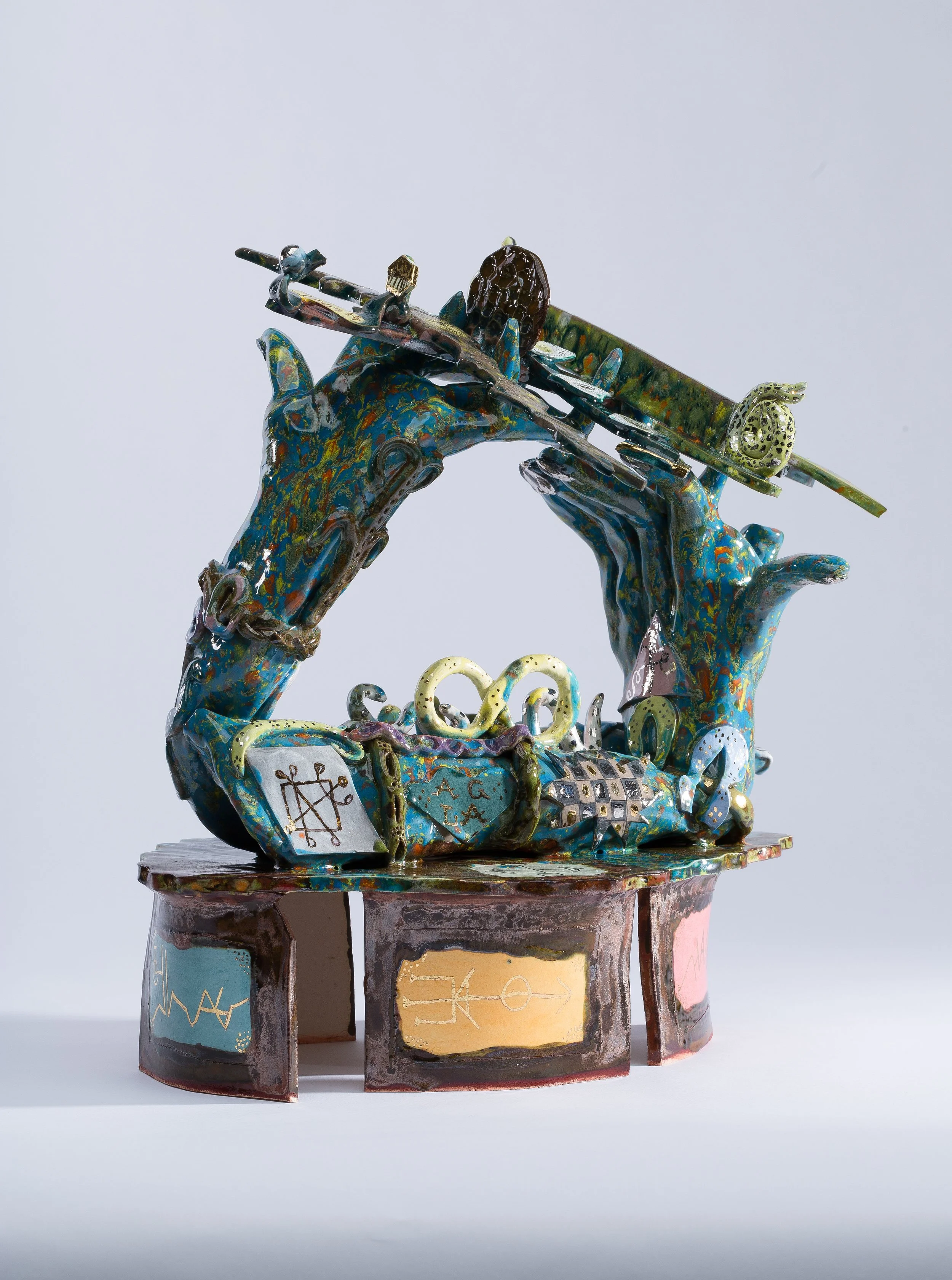 A colorful sculpture of two hands holding a musical instrument, decorated with various symbols and patterns, displayed on a stand against a plain background.