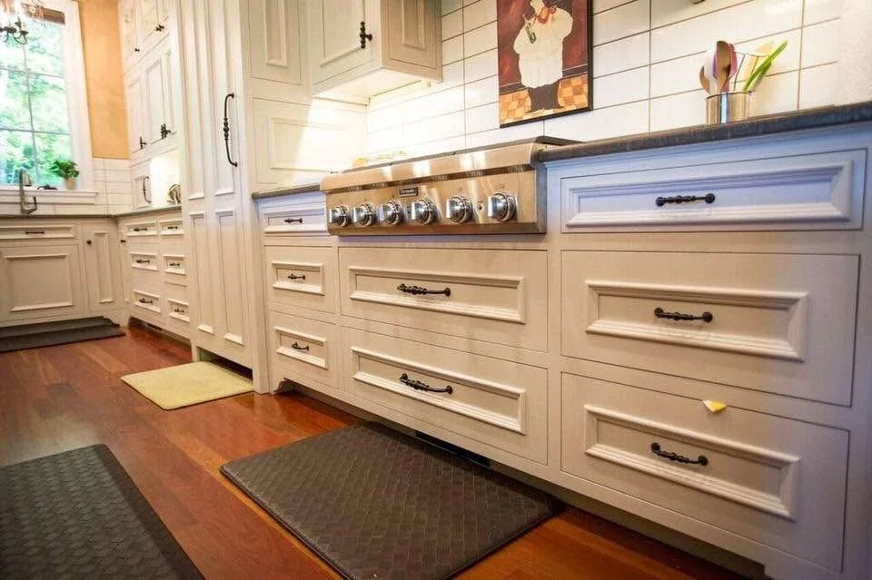 Kitchen with white cabinets, stainless steel oven, wooden floors, and two black mats on the floor.
