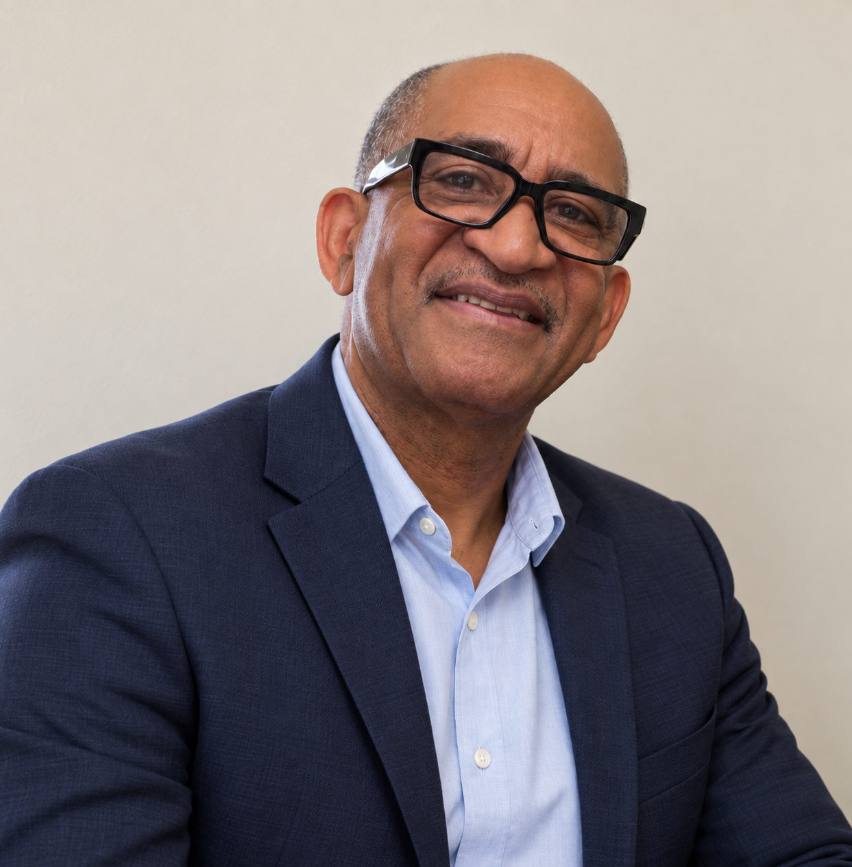 Portrait of a middle-aged man wearing glasses, a blue suit, and a light blue shirt, smiling against a plain light background.