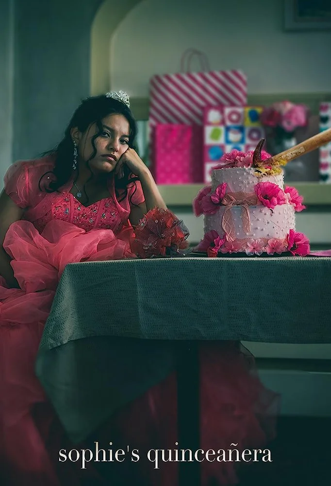 A young girl in a pink princess dress sitting at a table with a large, layered pink birthday cake decorated with pink flowers, with a serious or bored expression on her face.