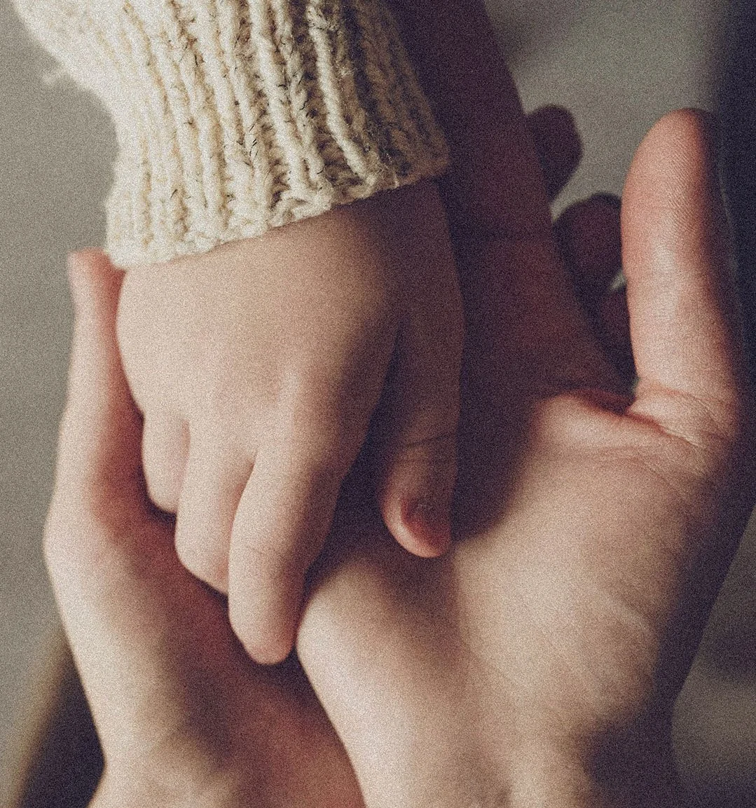 Close-up of two hands holding each other, one of which is wearing a knitted sleeve.