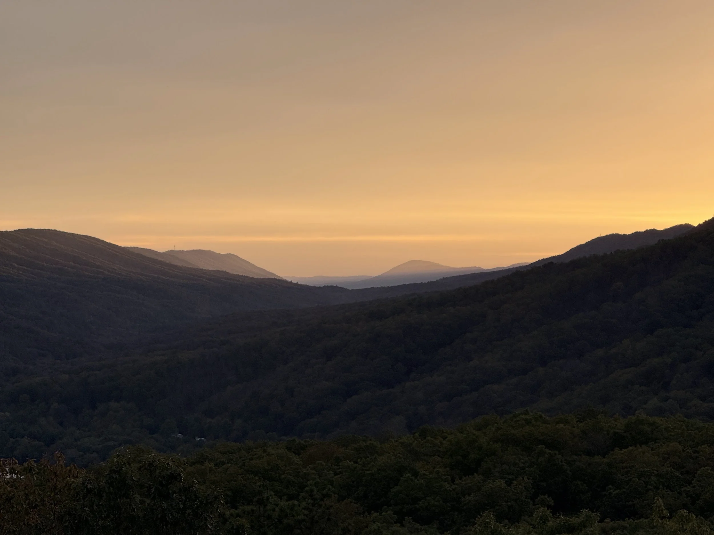 A landscape view of rolling hills under a colorful sunset sky, with muted orange and purple hues.