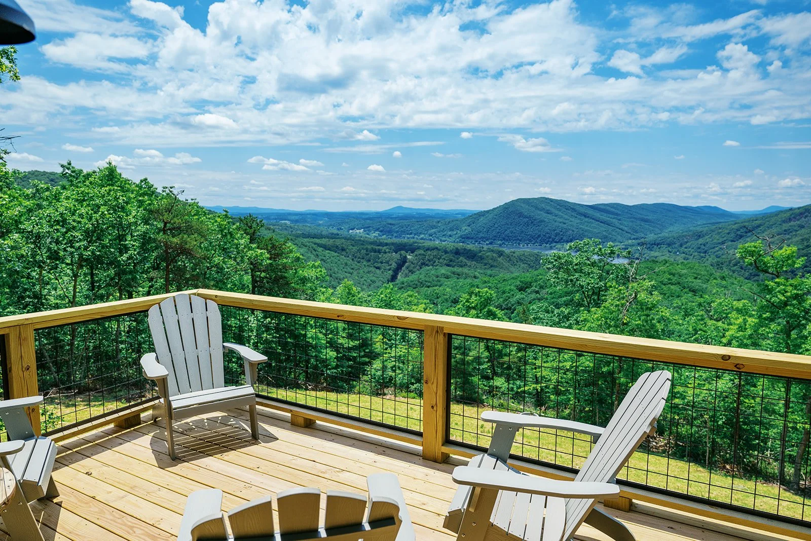 View from a wooden deck with Adirondack chairs overlooking a lush, green mountain landscape with a partly cloudy sky.