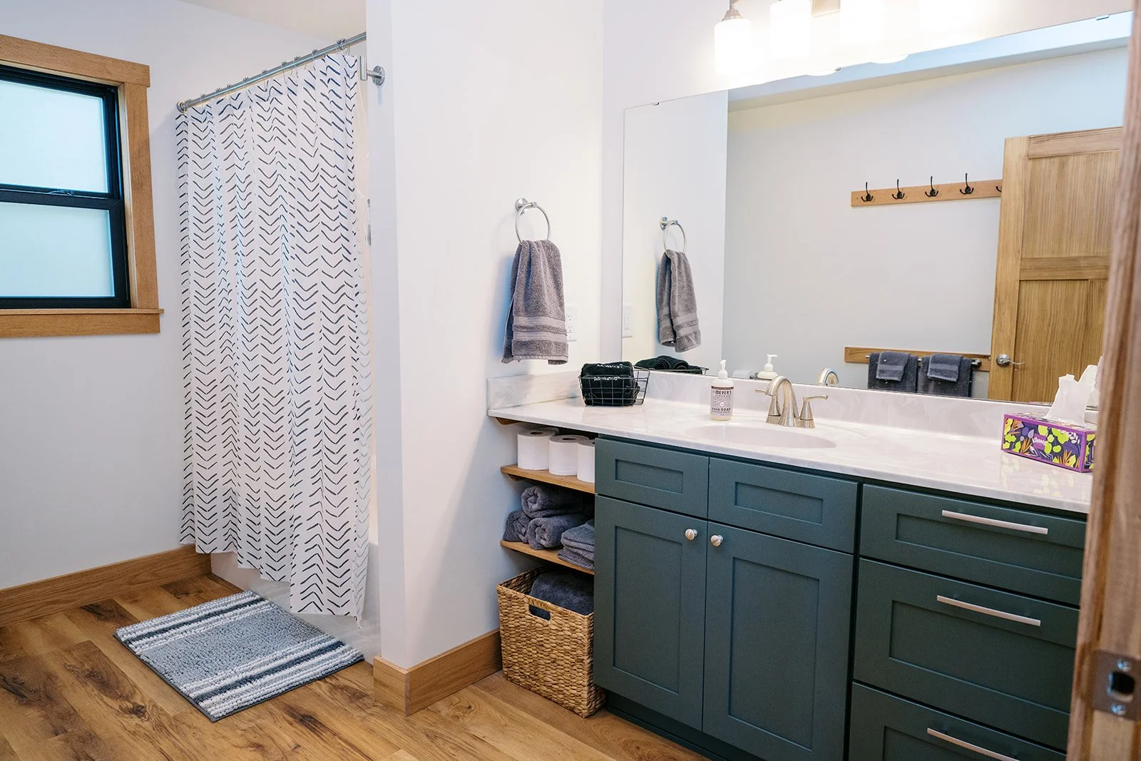 Bathroom with a green vanity, large mirror, towels, and a shower with a patterned curtain.