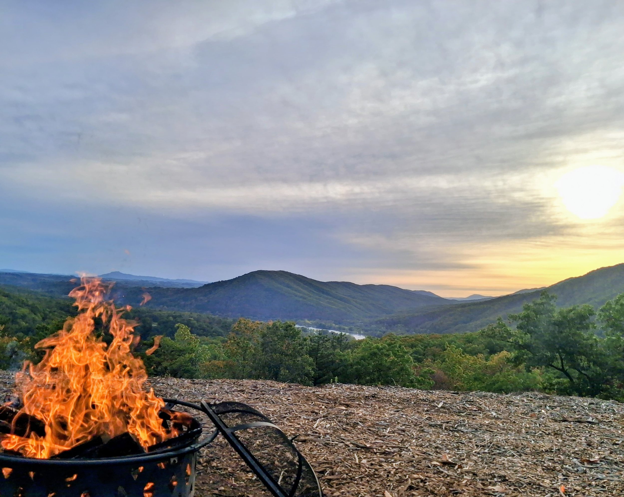 A campfire on a rocky surface with a mountain landscape and clouds in the sky during sunset.