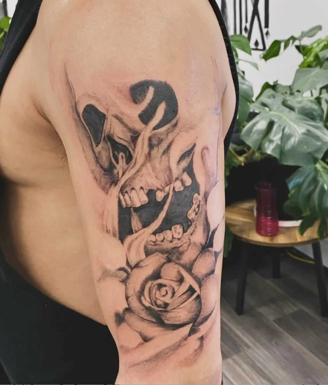 A black and gray tattoo on a person's upper arm depicting a skull intertwined with a rose and a snake.