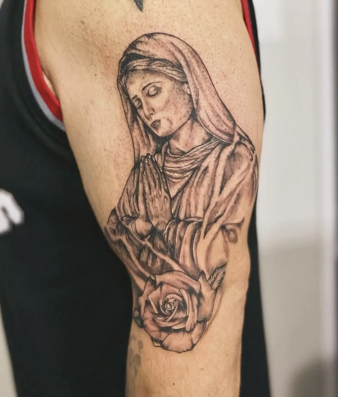 Tattoo of the Virgin Mary with hands in prayer, located on person's upper arm.